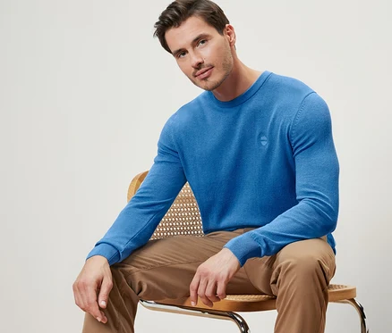Mann sitzt auf einem Stuhl und trägt einen blauen Pullover mit Rundhalsausschnitt.
