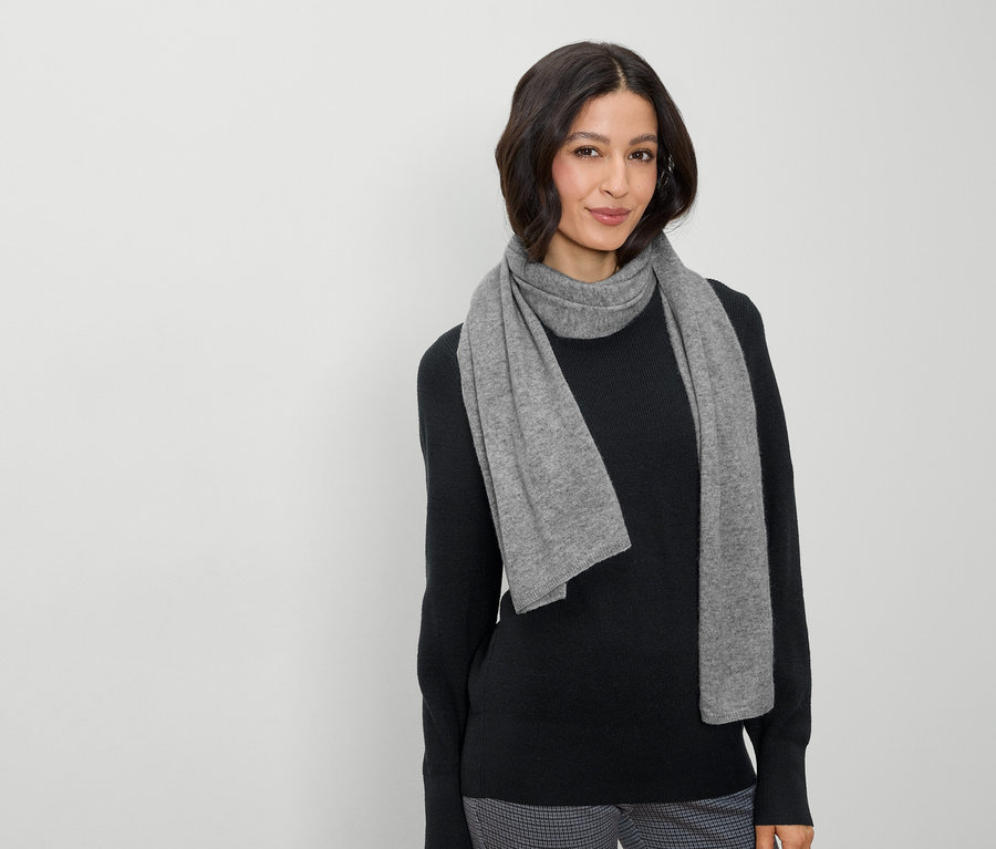 Eine Frau mit braunen Haaren und einem grauen Schal posiert vor einem hellen Hintergrund.