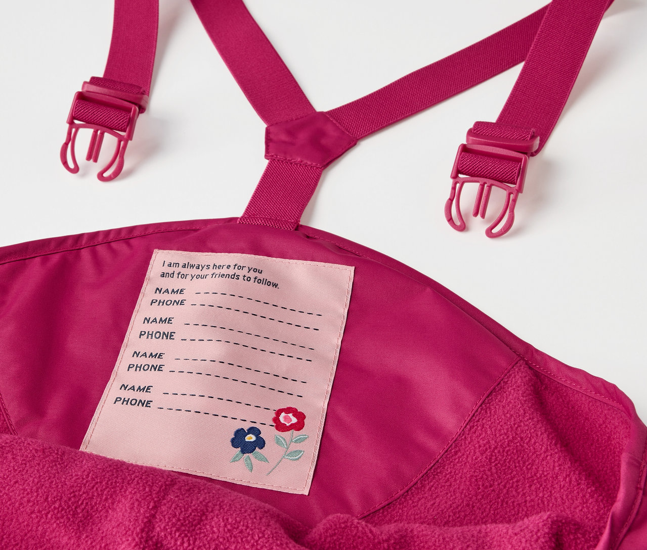 Detail der Kinder-Thermo-Regenhose in Beere mit Latz und Namensschild.