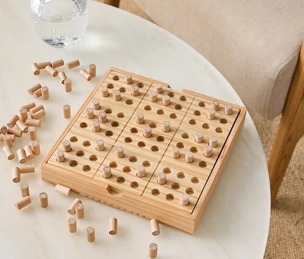 Holzspiel mit Stiften auf einem Tisch neben einem Glas Wasser.