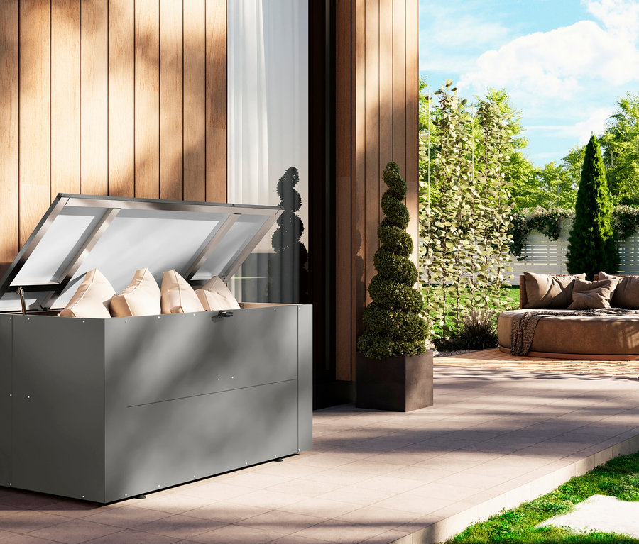 Auf einer Terrasse steht eine geöffnete Karibu Aluminium-Auflagenbox 1, Breite ca. 142 cm, im Hintergrund eine Sitzgelegenheit.
