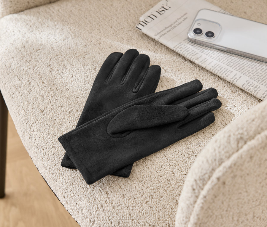 Auf einem beigen Stuhl liegen ein Paar schwarze Lederhandschuhe, eine Zeitung und ein Mobiltelefon.