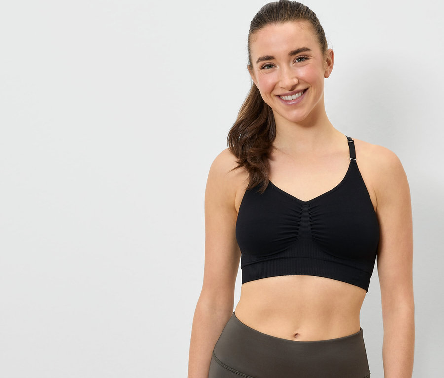Lächelnde Frau trägt einen schwarzen Sport-BH und graue Leggings.