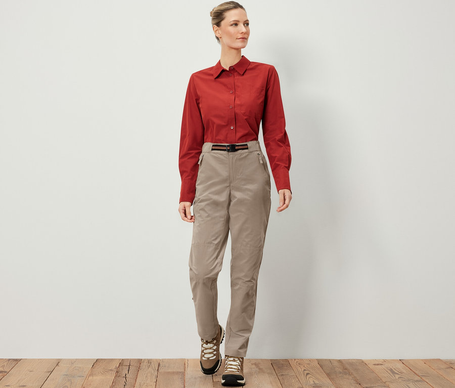 Frau trägt eine Outdoorhose mit Moskito-Schutz, ein braunes Hemd und Wanderschuhe.