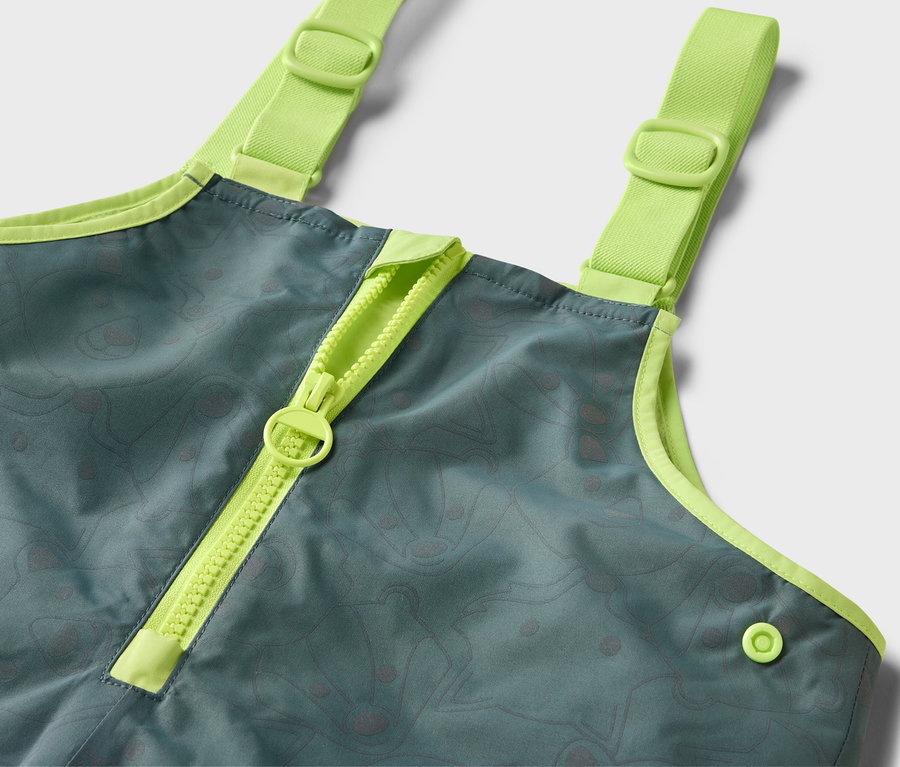 Detail einer Kinder-Thermo-Regenhose mit reflektierenden Elementen, mit neongrünem Reißverschluss und Trägern.