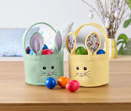 Zwei österliche Hasenkörbchen, eines mintgrün und eines gelb, gefüllt mit bunten Eiern, stehen auf einem Tisch.