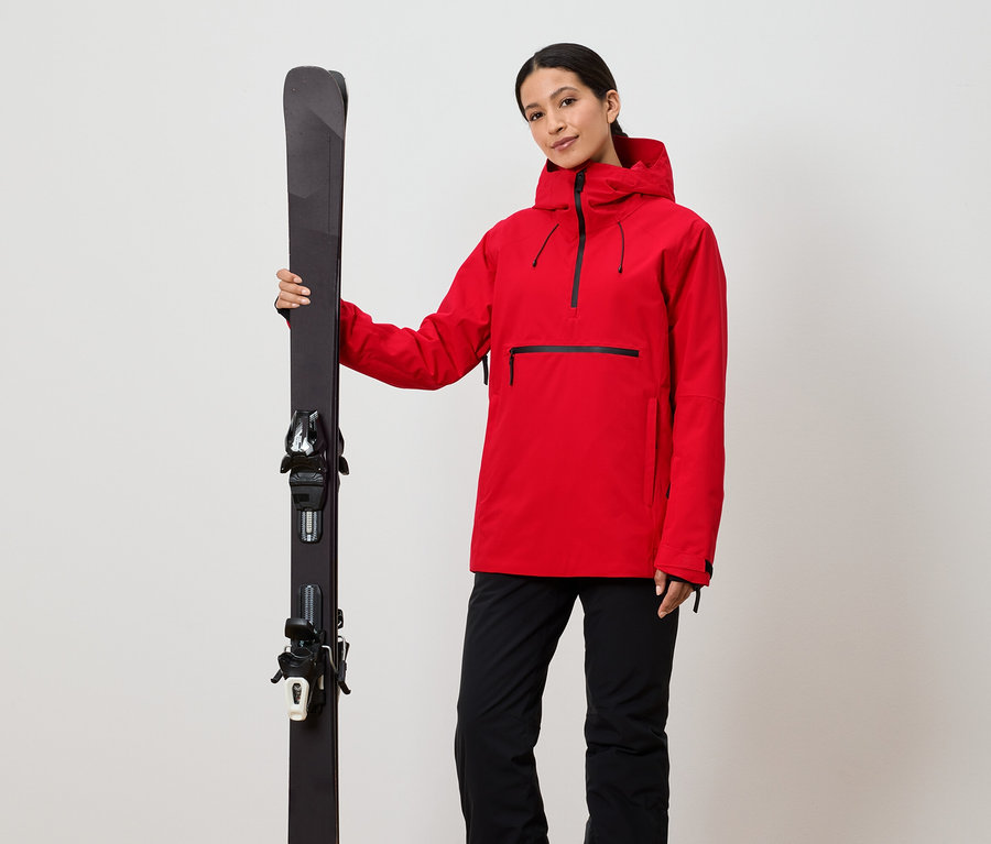 Frau hält Ski in roter Jacke und schwarzer Hose.
