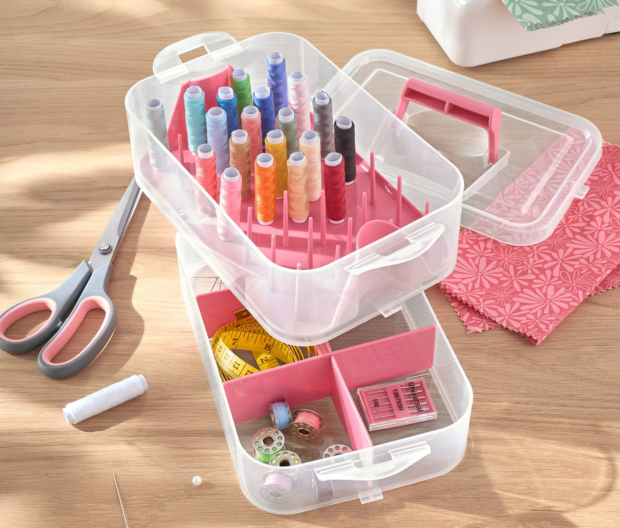Geöffneter Utensilienbox, Kunststoff mit Fäden, Schere, Nadeln und Nähmaschine auf einem Tisch.