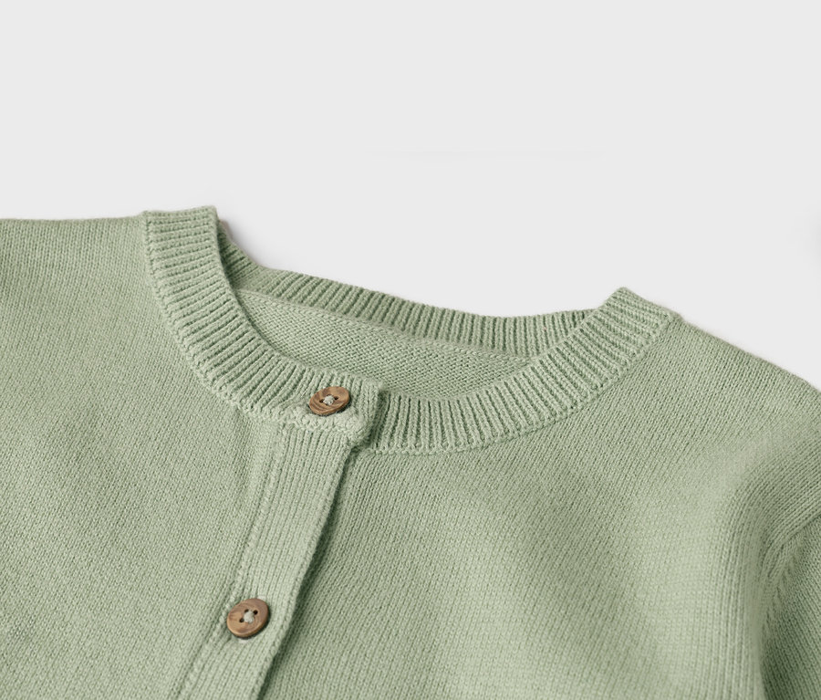 Nahaufnahme einer hellgrünen Strickjacke mit zwei Holzknöpfen.