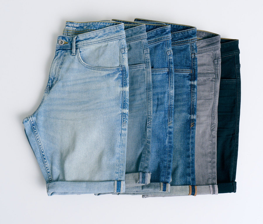 Sechs Jeanshosen in verschiedenen Blautönen, Grau und Schwarz liegen nebeneinander auf einem weißen Hintergrund.
