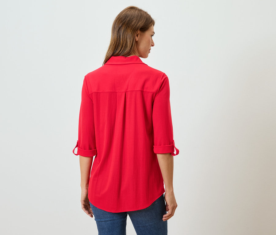 Rückansicht einer Frau mit langen braunen Haaren, die eine rote Langarmbluse und Jeans trägt.