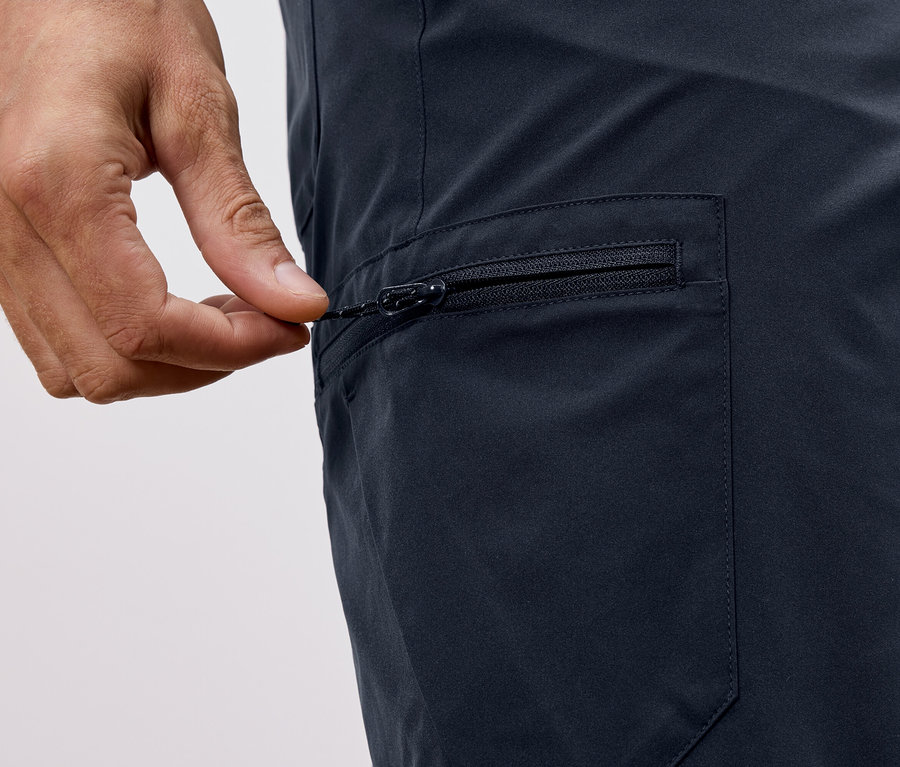 Nahaufnahme einer Hand, die den Reißverschluss einer marineblauen Hose schließt.