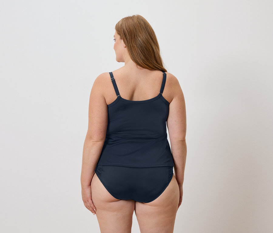 Rückansicht einer Frau mit langen braunen Haaren, die ein marineblaues Tankini-Top und eine Badehose vor einem weißen Hintergrund trägt.