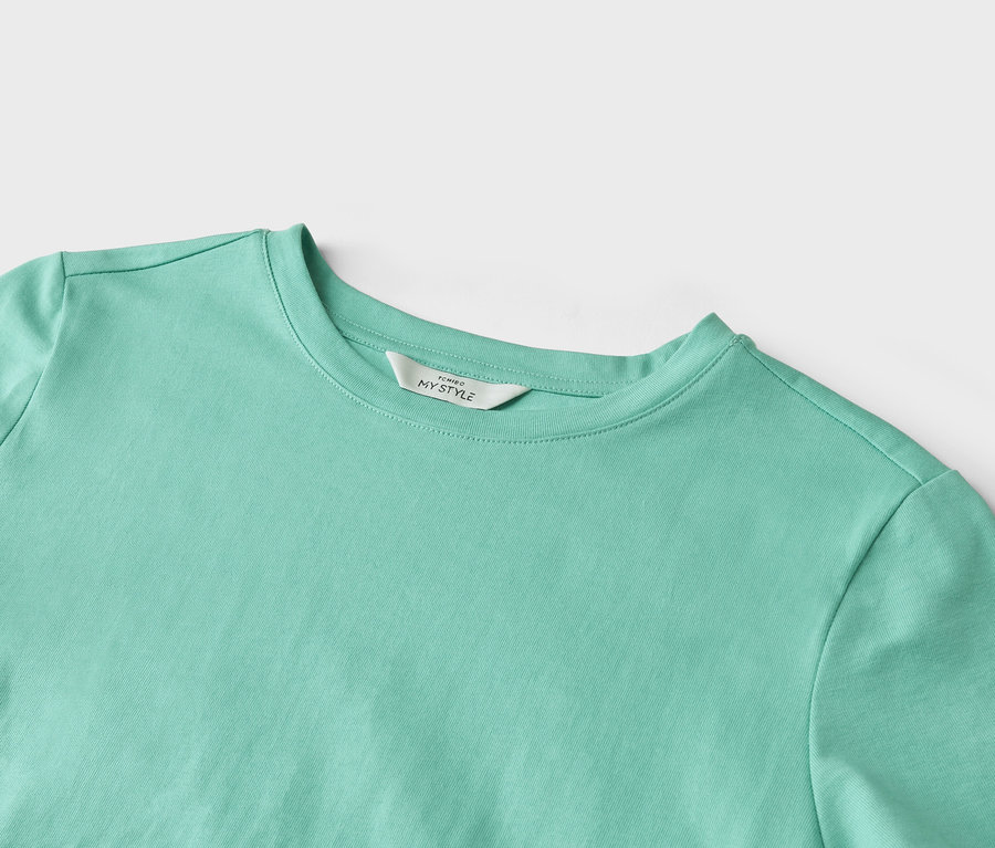 Nahaufnahme eines helltürkisfarbenen T-Shirts mit einem Etikett mit der Aufschrift "TCHIBO MY STYLE".