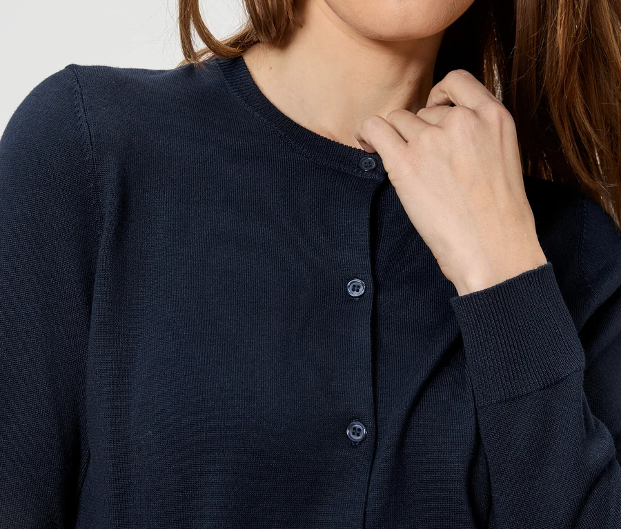 Frau berührt ihren Hals und trägt eine dunkelblaue Strickjacke mit Knöpfen.