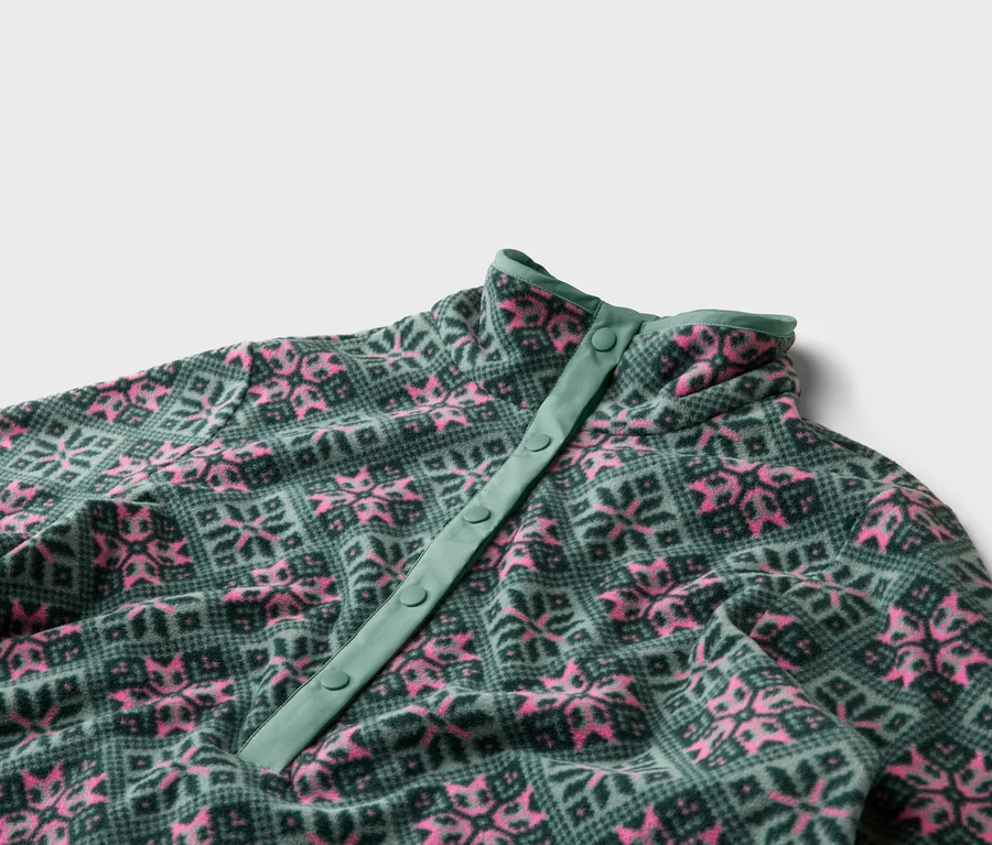 Nahaufnahme eines Fleecepullovers mit Knopfleiste, grünem Muster und rosa Schneeflocken.