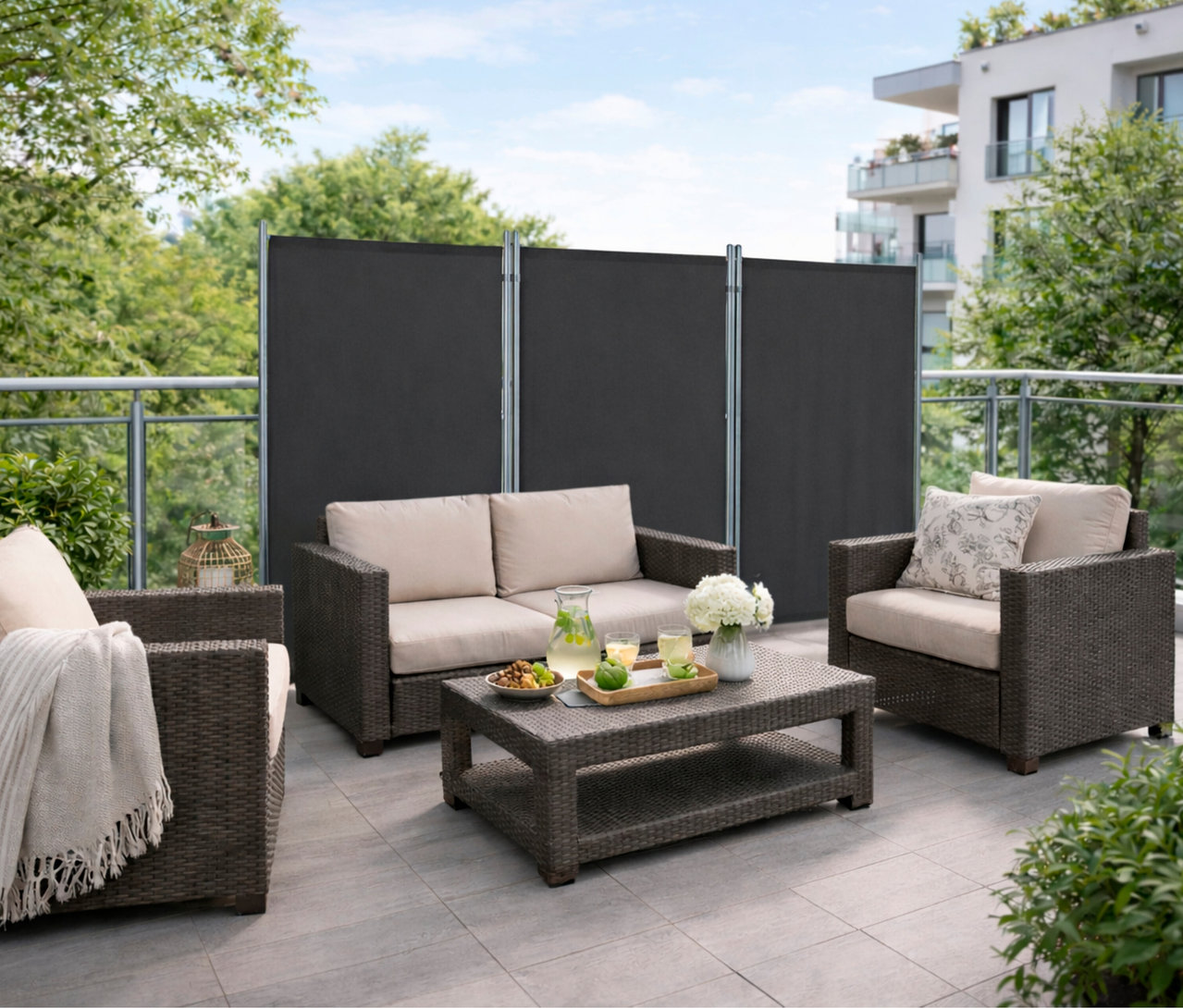 Auf einer Terrasse steht eine anthrazitfarbene, 3-teilige Leco Stellwand hinter einem Sofa und zwei Sesseln.