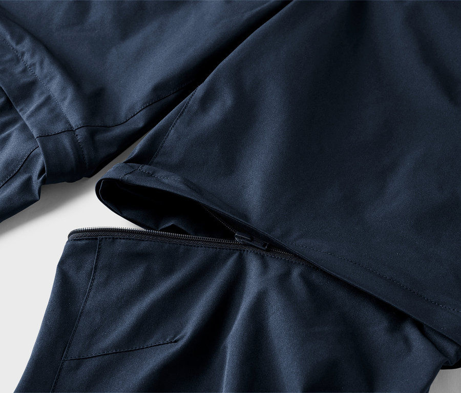 Detailansicht einer dunkelblauen Hose, bei der ein Hosenbein abzippbar ist.