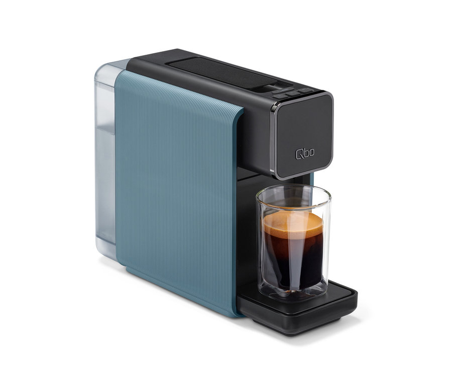 Eine Qbo ONE Kapselmaschine in Misty Blue und Dunkelgrau, die eine Tasse Kaffee mit Crema zubereitet.