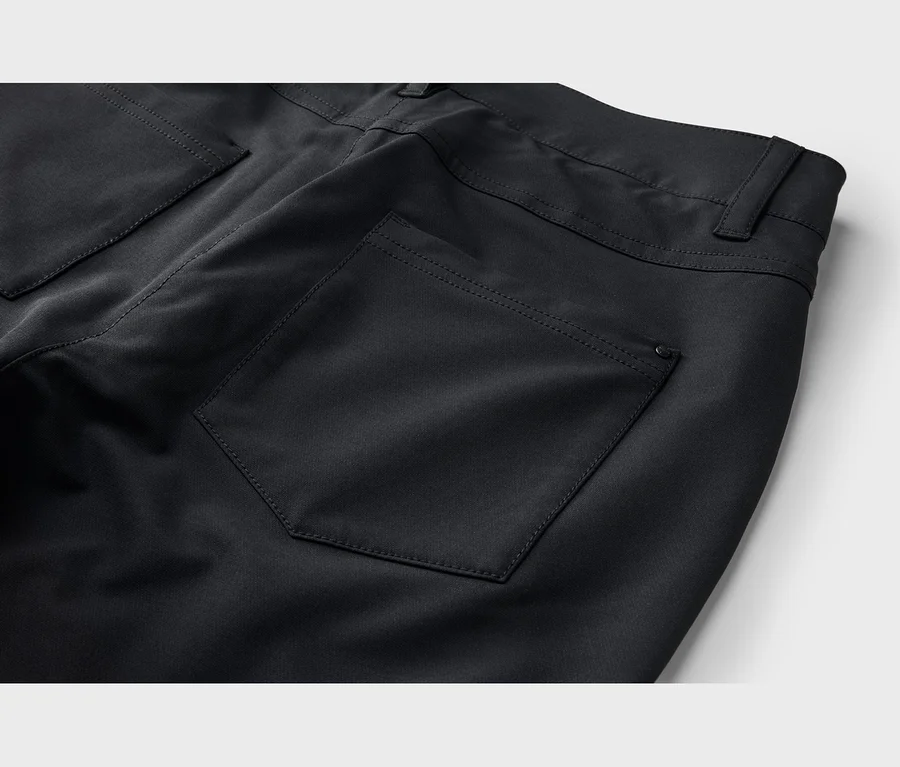 Nahaufnahme der Rückseite einer schwarzen Hose, die eine rechteckige Gesäßtasche mit sichtbaren Nähten, ein kleines schwarzes Logo-Etikett an der Tasche und einen Teil des Bundes mit einer Gürtelschlaufe zeigt.