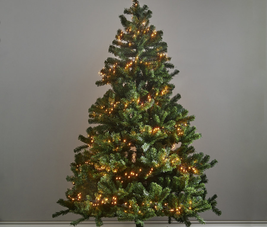 Grüner, beleuchteter Weihnachtsbaum mit warmweißen Lichtern und goldenen Geschenken darunter vor einer grauen Wand.