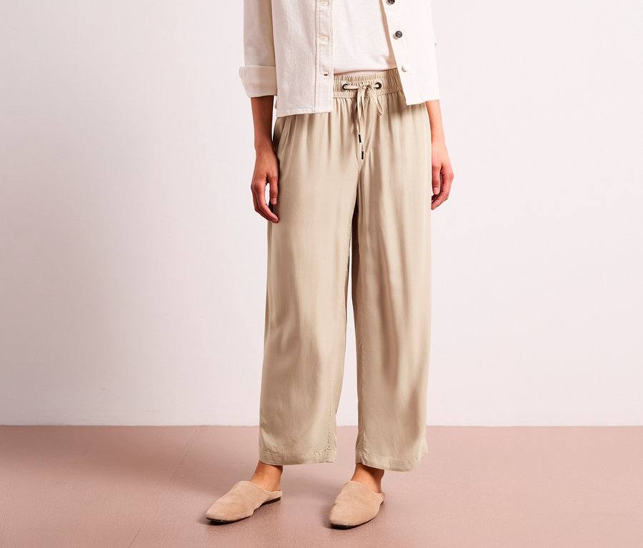Eine Person trägt eine beige Street One 7/8-Culotte, ein weißes Hemd und beige Hausschuhe.