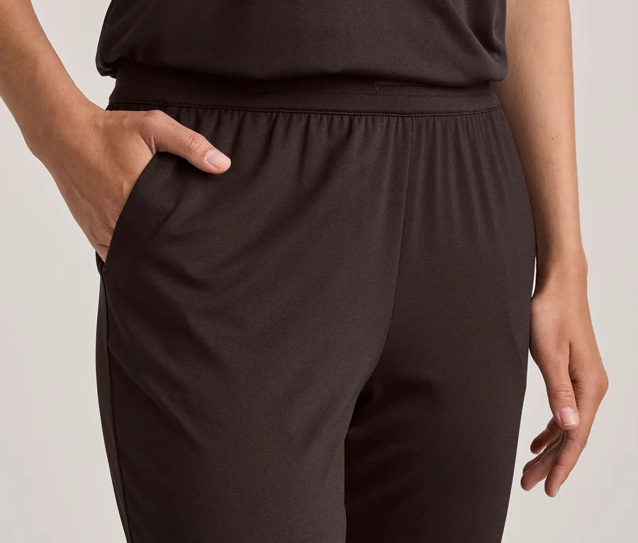 Eine Person trägt eine dunkelbraune Hose mit Gummibund; die linke Hand steckt in der Hosentasche, die rechte Hand ist daneben sichtbar.