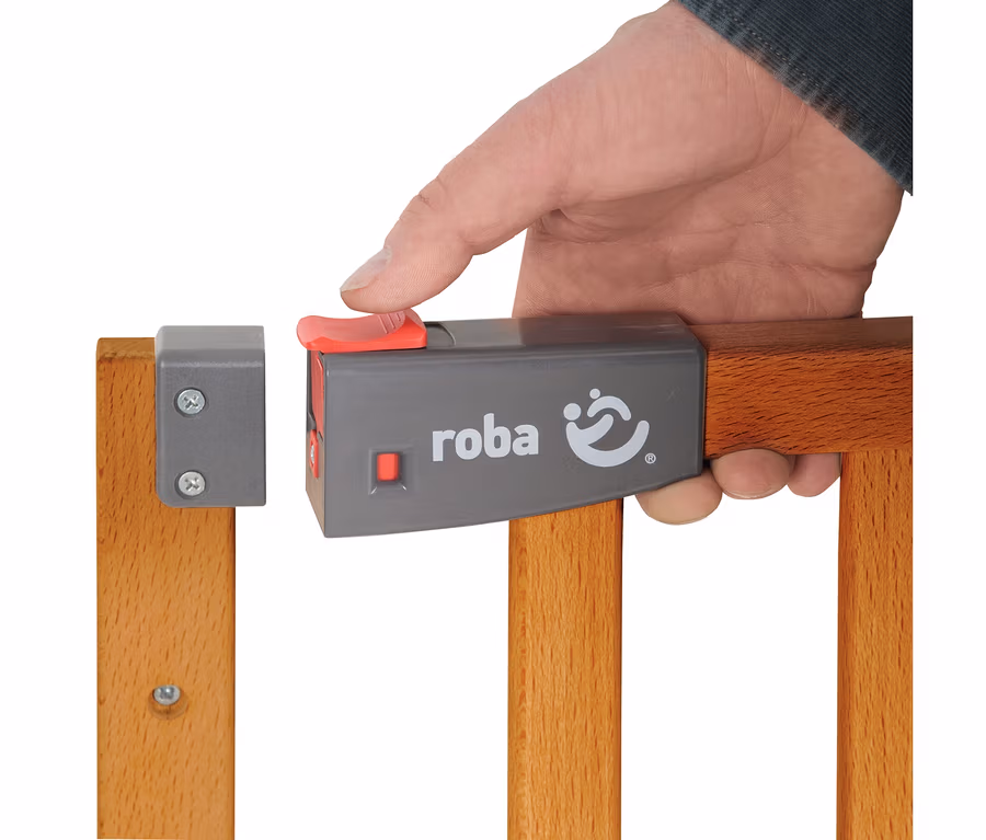 Hand betätigt den roten Verschluss des roba Türschutzgitters #Safety Up# aus Holz.