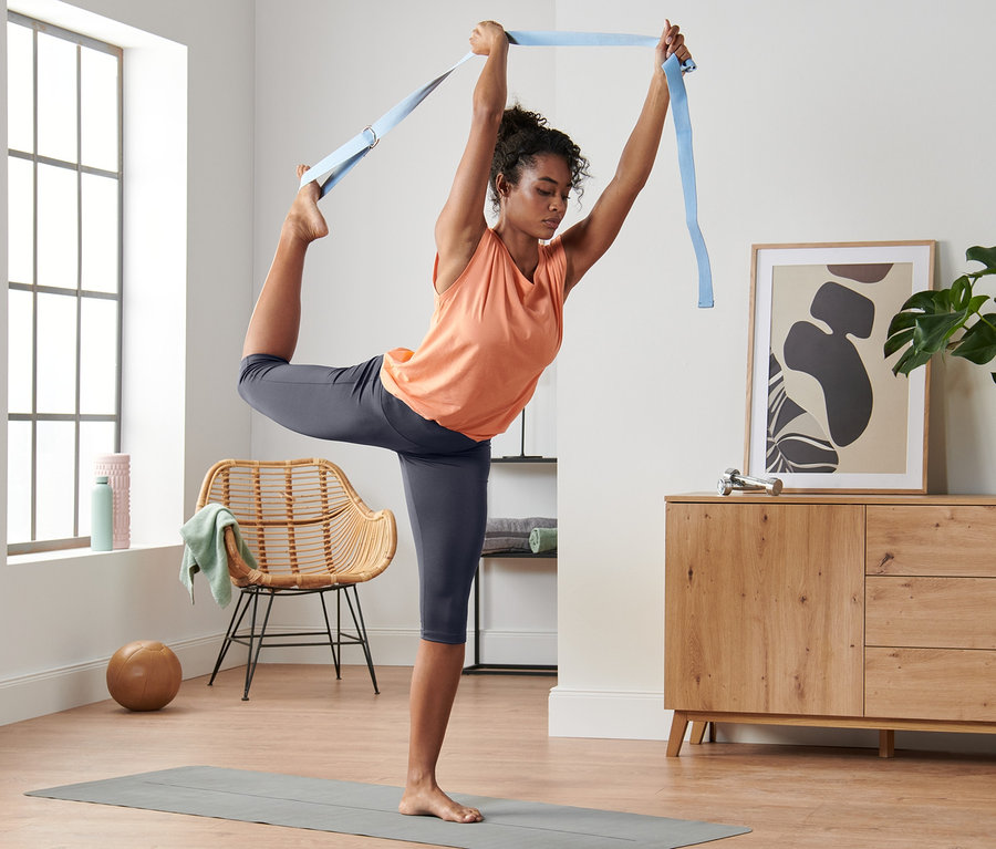 Frau macht Yoga mit einem Gurt auf einer Matte und trägt eine Super-Soft-3/4-Sporttight.