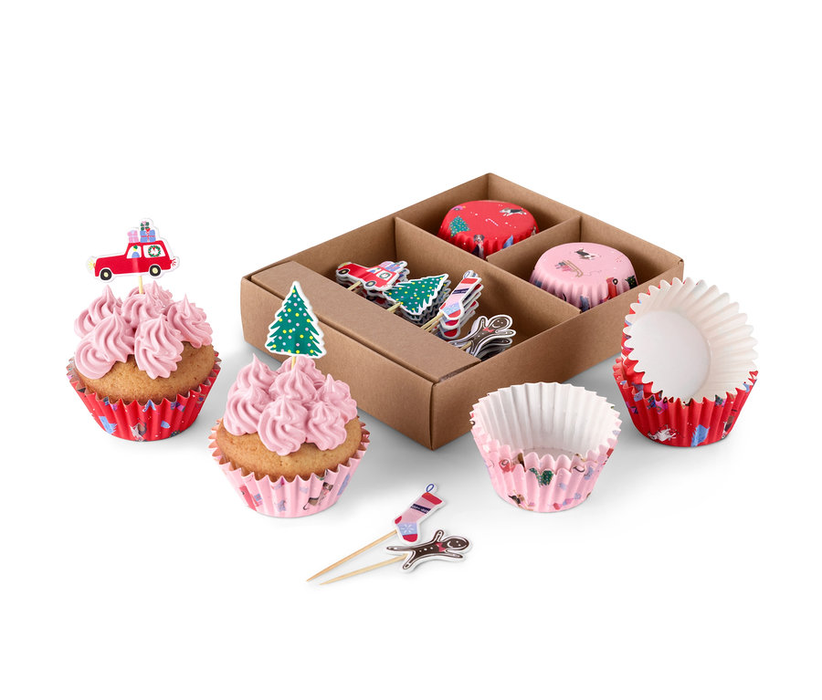 Zwei mit rosa Creme und Weihnachtsdekoration verzierte Muffins neben einem Muffin-Deko-Set.