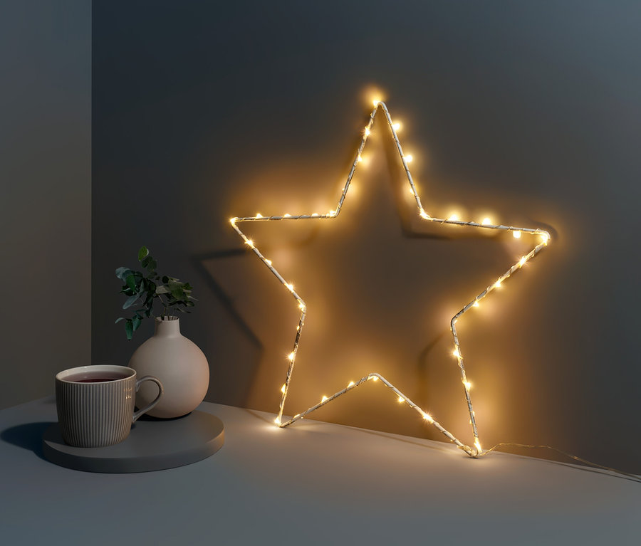 Kleiner LED-Metallstern steht neben Tasse und Vase auf einem Tisch.