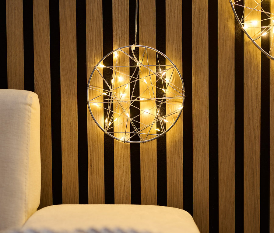 Zwei kleine LED-Kreise hängen an einer Holzwand über einem Sofa.