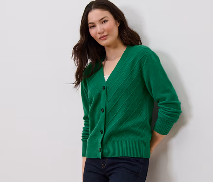 Eine Frau posiert in einem grünen Cardigan mit Strickstruktur und dunkelblauen Jeans.