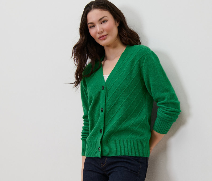 Eine Frau posiert in einem grünen Cardigan mit Strickstruktur und dunkelblauen Jeans.