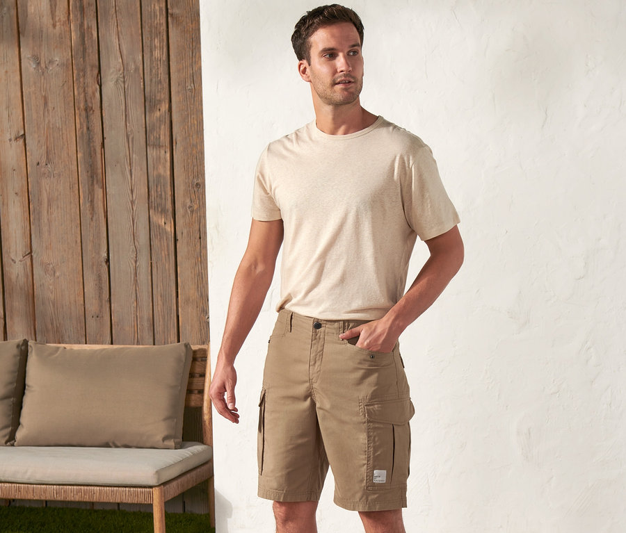 Ein Mann steht draußen und trägt ein beiges T-Shirt und khaki Shorts »Workwear«.