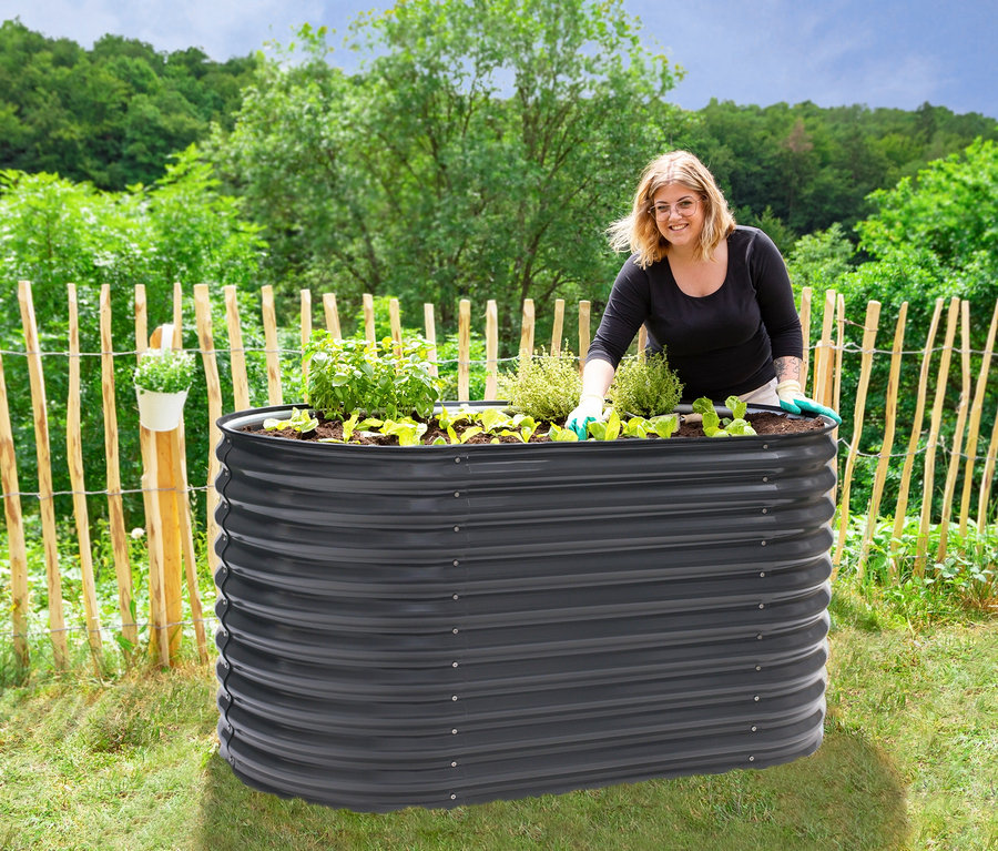Frau setzt Setzlinge in ein ovales Hochbeet mit einer Breite von ca. 160 cm.