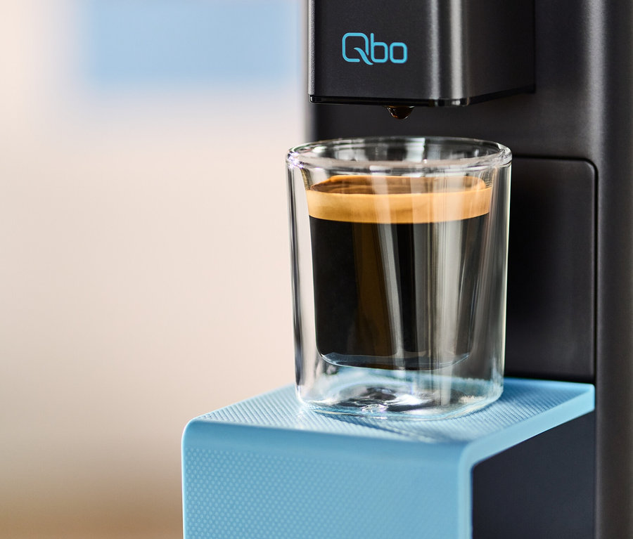 Kaffee läuft aus der Qbo ICONIC x Pantone Special Edition Sky Blue Kaffeemaschine in ein Glas.