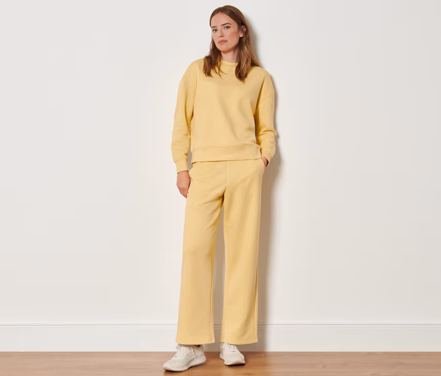 Eine Frau steht und trägt eine gelbe Sweatpants und ein Sweatshirt.