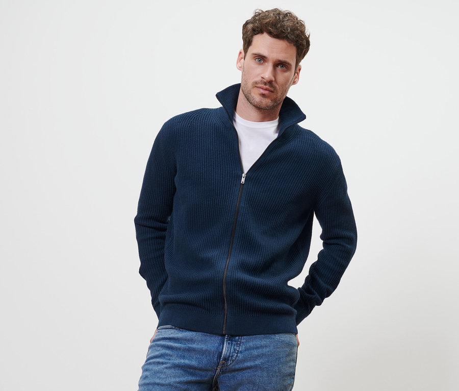 Mann posiert im marineblauen Strickjacke und Jeans.