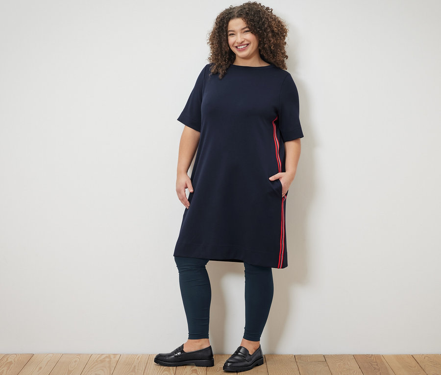 Frau posiert in einem Sweatkleid mit Galonstreifen und Leggings.