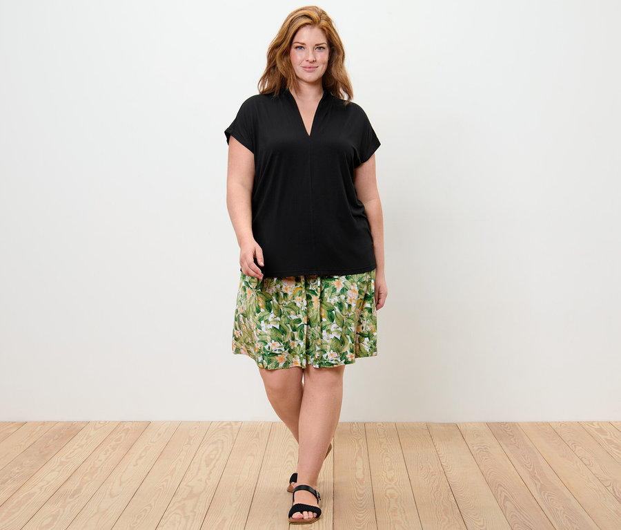 Frau trägt ein Blusenshirt mit V-Ausschnitt und einen bedruckten Jerseyrock.