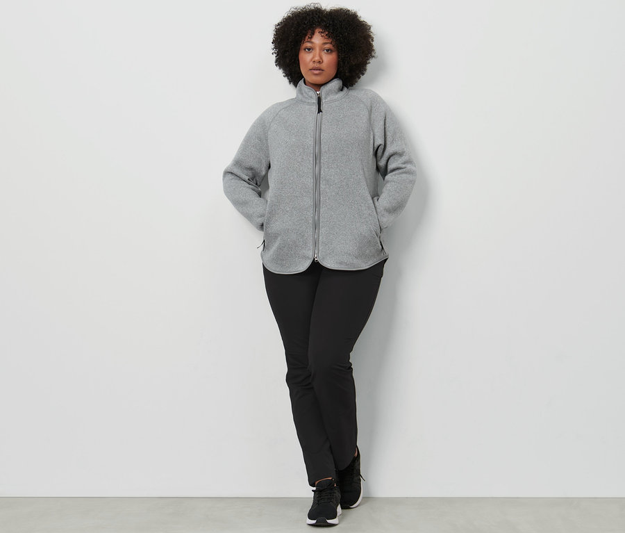 Frau posiert in hellgrauer Strickfleece-Jacke und Softshellhose.