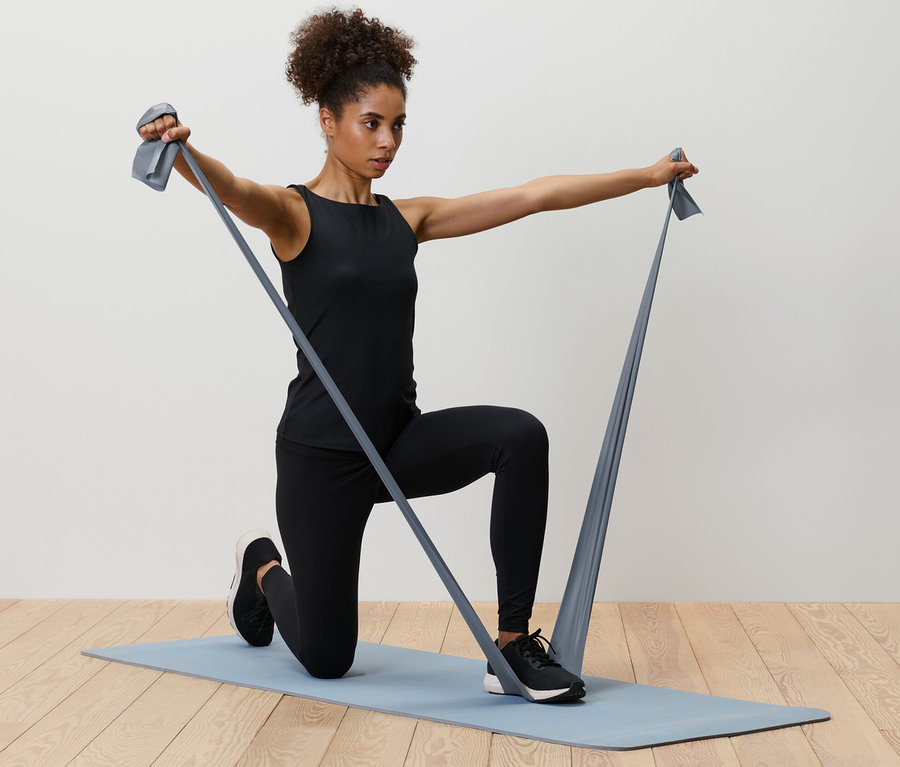 Frau kniet auf einer Matte und trainiert mit 2 Fitnessbändern.