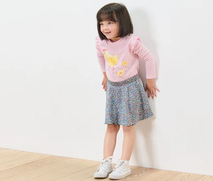 Mädchen steht an der Wand und trägt einen Kinder-Rock mit Hose.