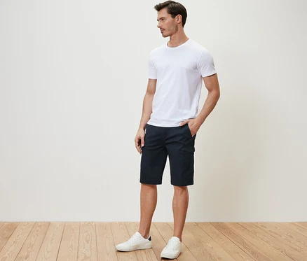 Mann steht seitlich mit der Hand in der Tasche der dunkelblauen Cargo-Shorts.