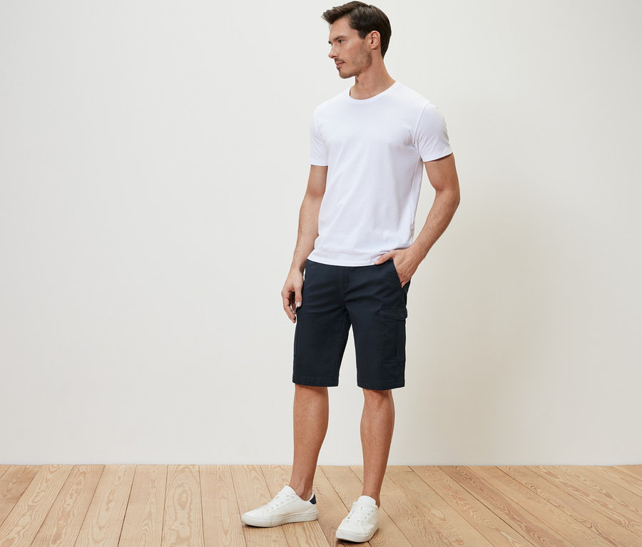 Mann steht seitlich mit der Hand in der Tasche der dunkelblauen Cargo-Shorts.