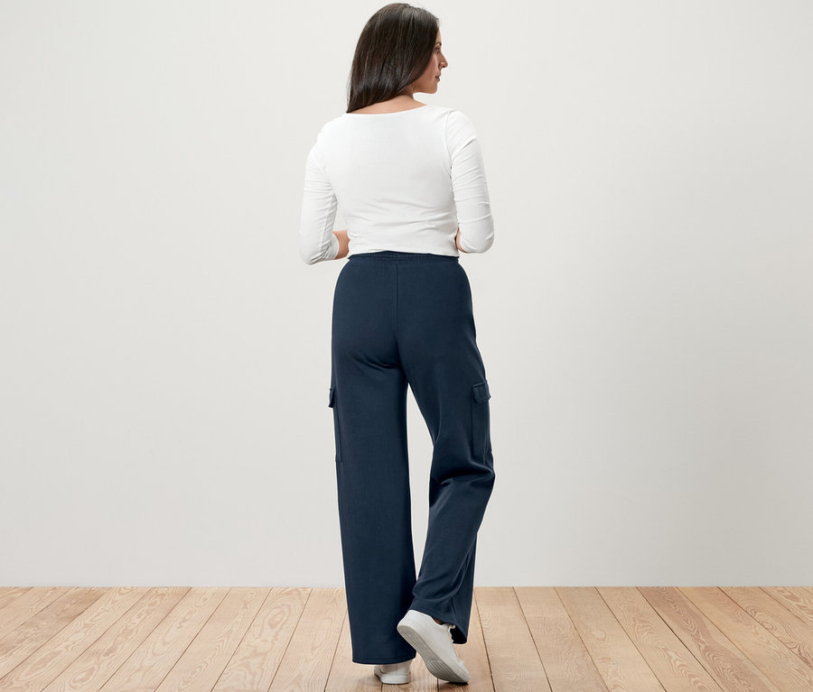 Frau steht mit dem Rücken zur Kamera und trägt eine dunkelblaue Sweathose mit Cargo-Taschen.