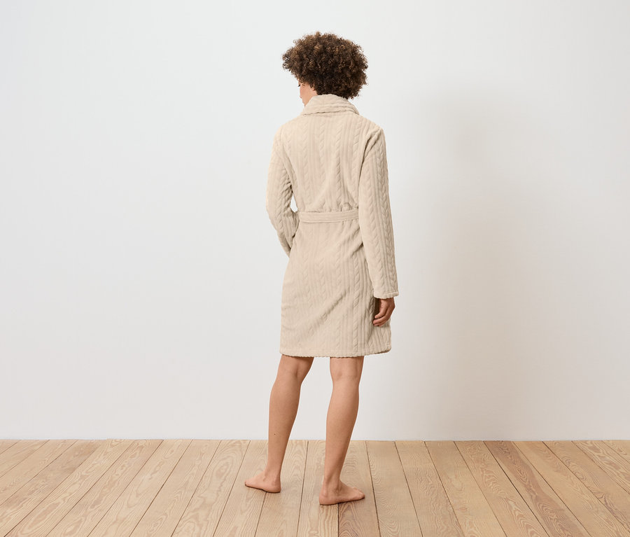 Frau von hinten in einem beigen Bademantel mit Zopfmuster.
