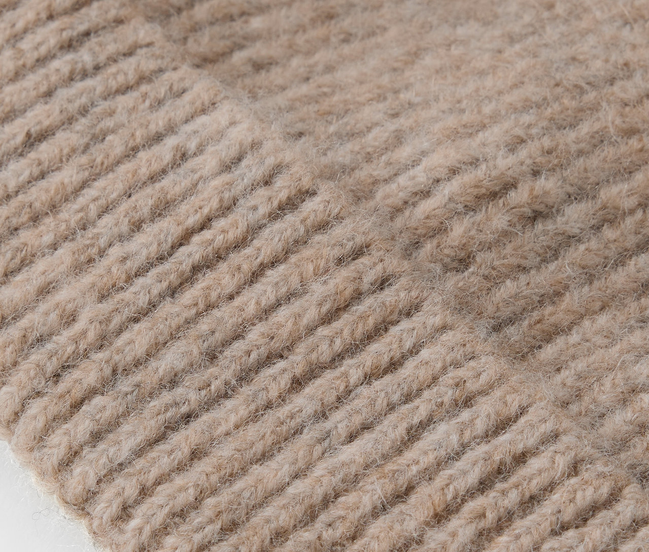 Detailaufnahme der Strickstruktur einer beigen Mütze.