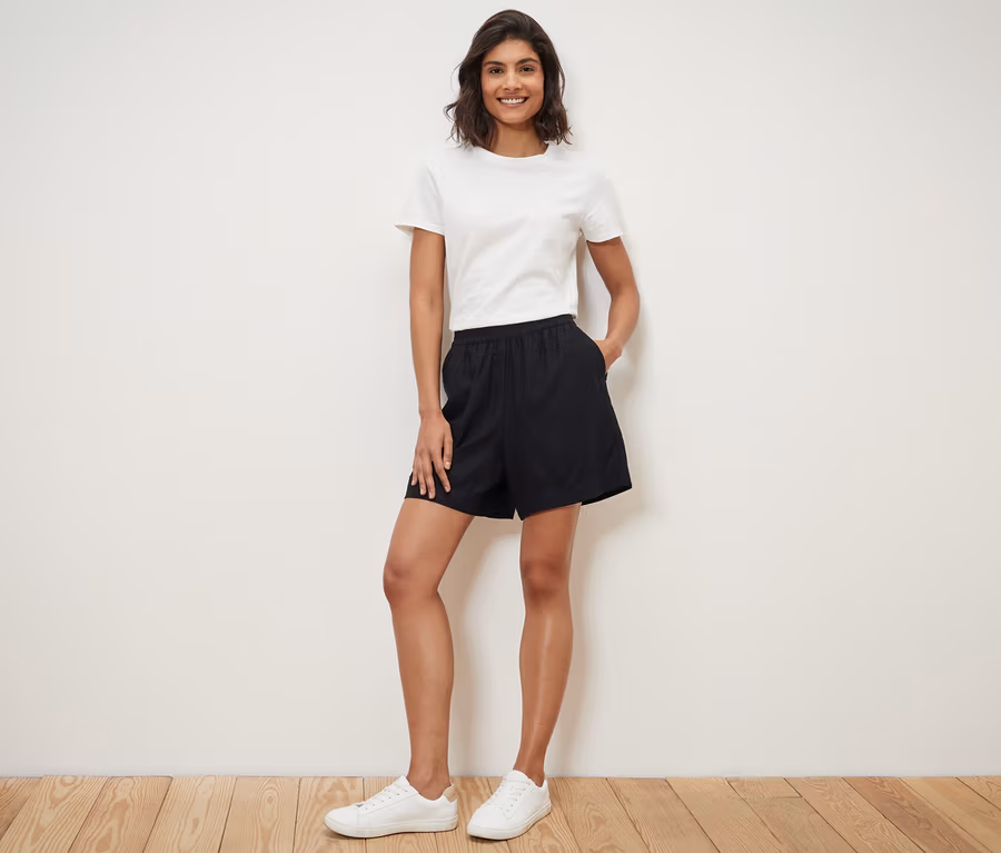 Frau steht mit Händen in den Taschen ihrer schwarzen Leinenshorts.